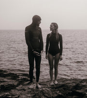 Nick and Sarah standing in wetsuits in front of the sea