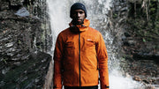 man wearing finisterre coat next to waterfall